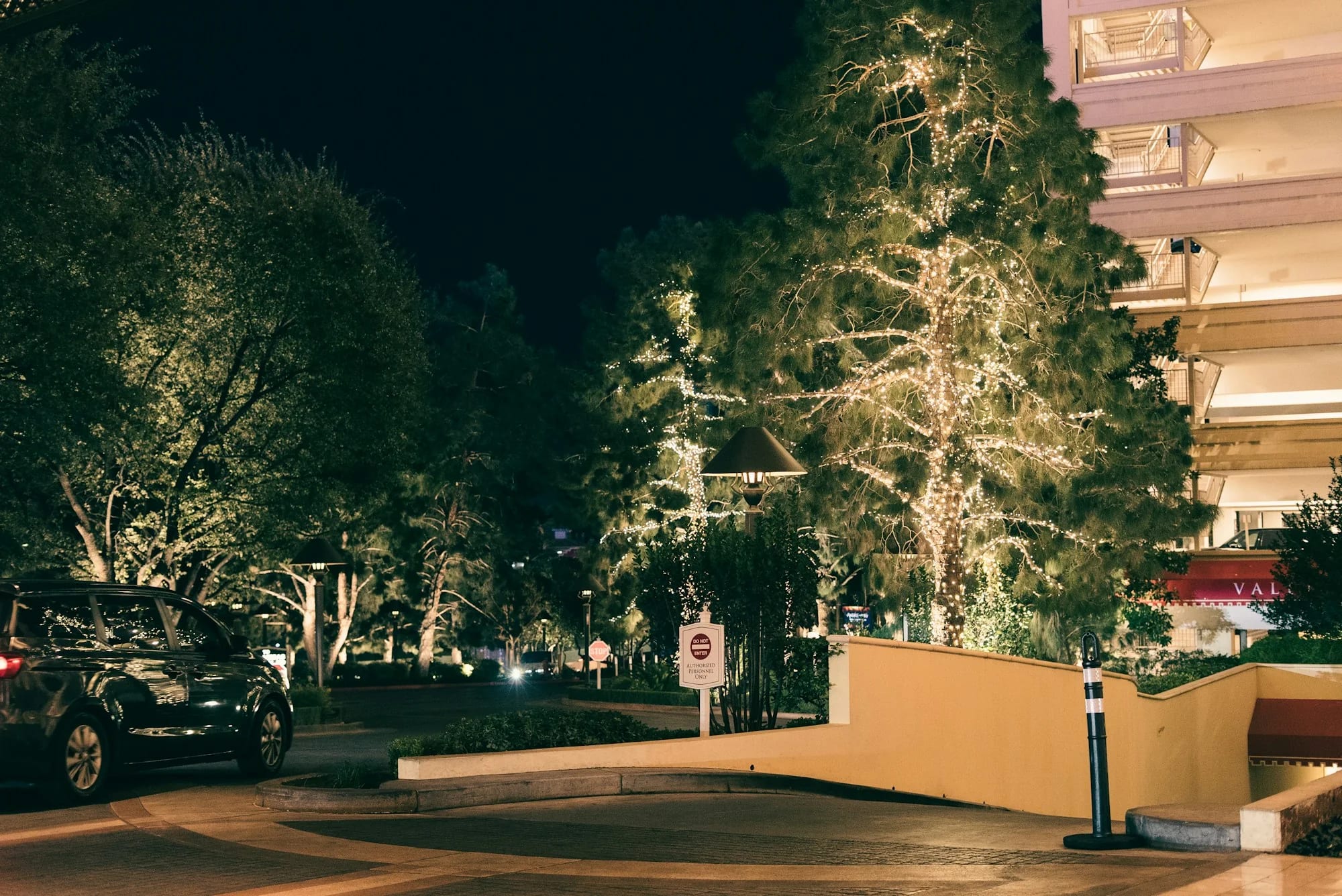 A dark vehicle arriving at a warmly illuminated hospitality entrance at night