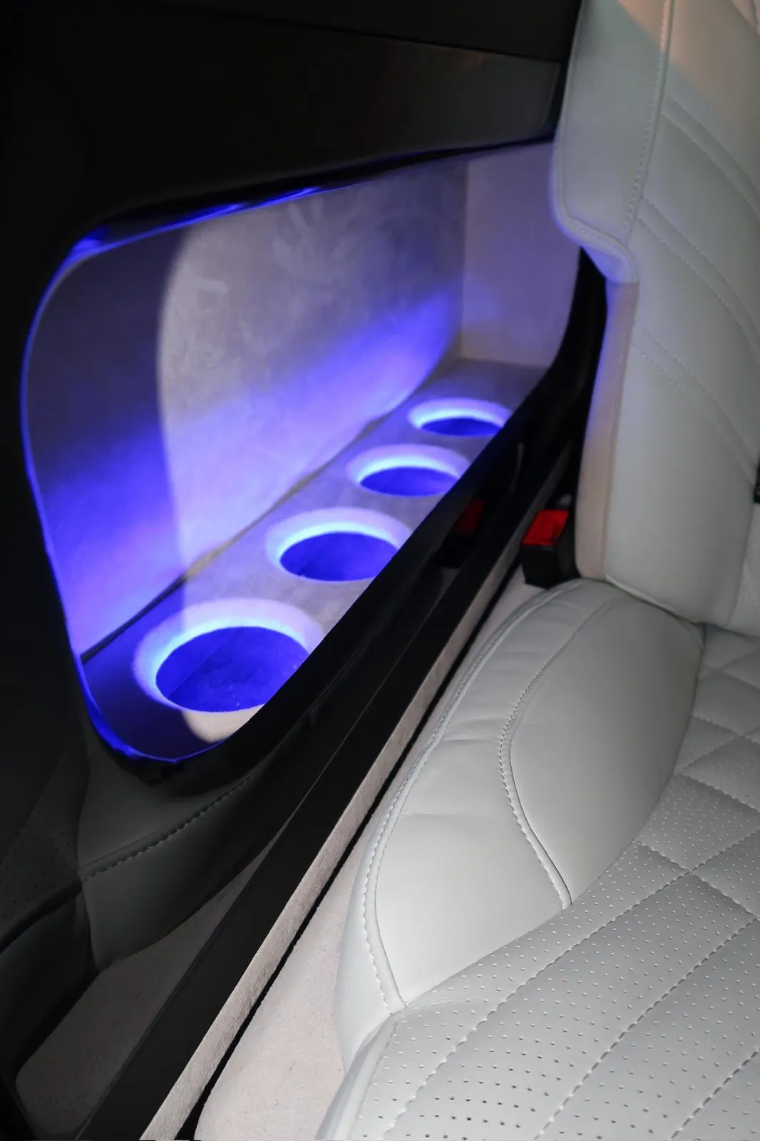 Blue-lit cupholders beside a white leather seat